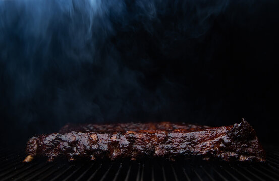 Smoke rolls off barbecue ribs slow cooking on a grill