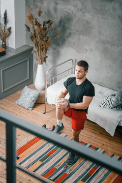 A Cheerful Athlete With Black  Hair  Lunges,  Stretching  In The Bedroom, Next To A Laptop With Online Training. The Young Man Goes In For Sports At Home.