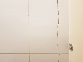 Cracks form a long path on the tile wall.