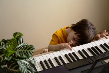 A boy tired of playing the synthesizer. Toddler learning how to play piano. Child's hands on the keyboard. Early development and education concept