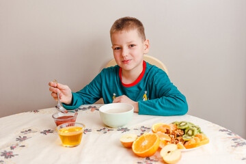 A nine-year-old boy in his pajamas sits at a table eating oatmeal with fruit. Healthy baby breakfast