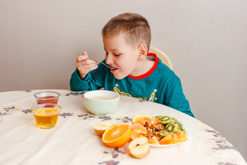 A nine-year-old boy in his pajamas sits at a table eating oatmeal with fruit. Healthy baby breakfast