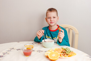 A nine-year-old boy in his pajamas sits at a table eating oatmeal with fruit. Healthy baby breakfast