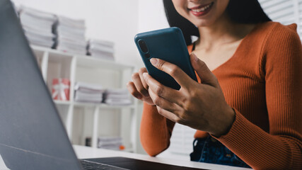 Close up Asian woman using phone and laptop, smile and looking at mobile smartphone in the room, feeling happy.