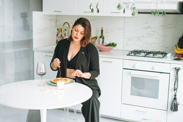 Beautiful sensual brunette young woman plus size body positive with dish of pasta and glass of wine on kitchen at the home