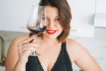 Beautiful happy sensual brunette young woman plus size body positive with glass of red wine enjoying her life at home