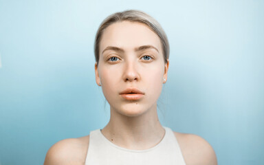 Beauty portrait of attractive young woman close-up. Blonde with big lips and clean skin on light blue background. Big blue eyes, black thick eyebrows