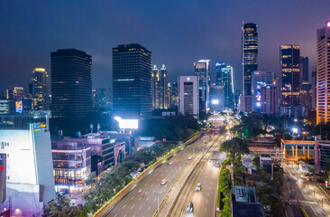 Fototapeta na wymiar View of fast night time traffic through modern urban city center with skyscrapers in Jakarta, Indonesia Aerial view of multi lane highway through the city