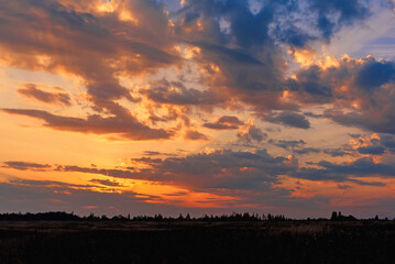 Golden orange sunset in the autumn night in cloudy sky over field and forest
