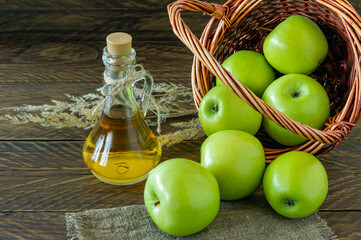 Wicker basket with ripe green apples and bottle of aplle vinegar on wooden background