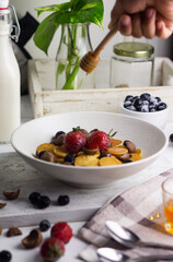 Cereal Pancakes or mini pancakes for breakfast, served with blueberries, strawberries and honey. Bright mood photography concept. White background. 