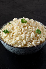 Rice in a bowl, cooked, garnished with fresh parsley, close-up on a black background