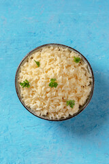 Cooked rice with fresh parsley leaves, overhead shot on a blue background with a place for text
