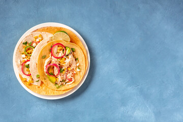 Tacos with chicken, cheese and avocado, shot from the top on a blue background with copy space