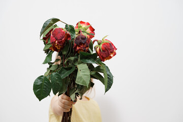 child holds out a bouquet of withered red roses