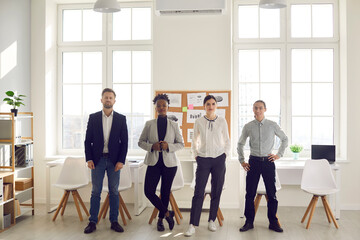 Team of four creative diverse business people looking at camera standing in modern workspace. Group...