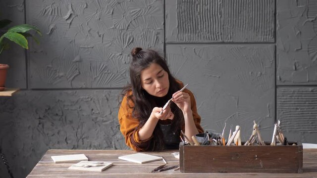 Pretty asian potter woman working on details of a clay handcraft piece. Work with different pottery tools. Concept of creative leisure time and ceramics. Start up small business, artwork and interior