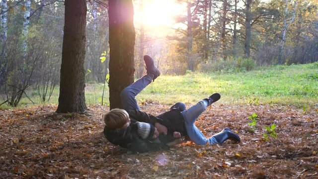 A teenager plays with a child, runs in the Park around a tree and catches up with him. The sun's rays penetrate the pine forest. Laughter and joy of the whole family.