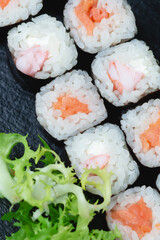 Sushi rolls with salmon, rice, eel and soy sauce on dark stone background