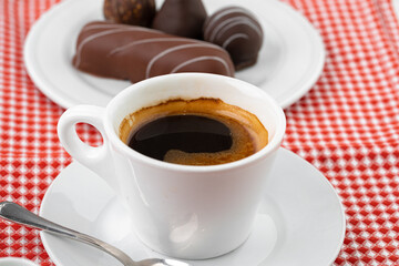 Cup of coffee and saucer with chocolate sweets on wooden table