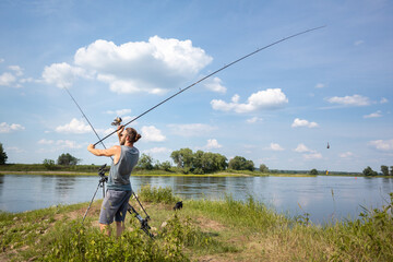 Man on a river bank casting a carp fishing rod on a warm summer day