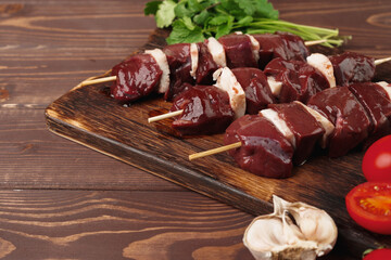 Raw beef liver kebab on skewers on wooden board
