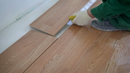 May laying laminate flooring at home. Installing laminated floor, detail on wooden tiles ready to be fit. Laying laminate flooring in a new apartment.