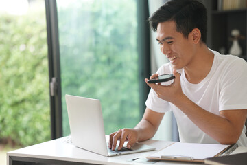 asian young student man entrepreneur talking on mobile phone woking with computer at home