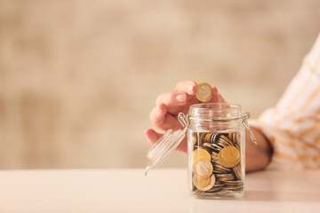 Senior woman putting coin in jar at table. Concept of pension - obrazy, fototapety, plakaty