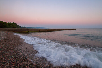 Waves run onto the seashore. Evening landscape with the moon.