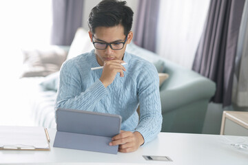 asian young student man entrepreneur working with tablet studying learning online at home. e-learning webinar meeting. social distance in covid pandemic