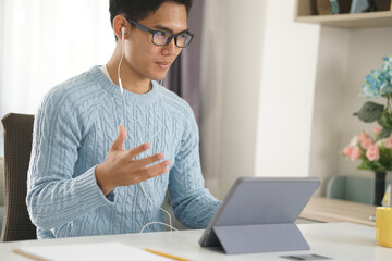 asian young student man entrepreneur wear earphones working by video call conference studying learning online at home. e-learning webinar meeting. social distance in covid pandemic