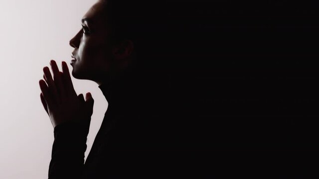Female silhouette. Sin confession. Forgiveness blessing. Dark contrast dramatic profile shape of grateful praying woman face hands isolated on white empty space background with black shadow.