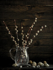 A bouquet of willow with flowers in a dark vase on a dark background.