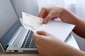 Envelope with euro banknotes in female hands. Woman pulls money out of an envelope on laptop...