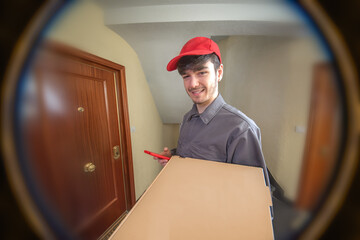 Delivery man delivering food order, pizza in cardboard box, seen through the peephole - obrazy, fototapety, plakaty