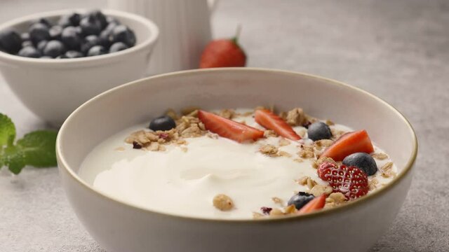 Girl scoops yogurt with berries and granola with a spoon. Close-up 