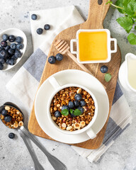 Homemade granola made from buckwheat. Organic buckwheat granola, green buckwheat sprouts, hazelnuts, pumpkin seeds, flax seeds and nutmeg. Granola in a white plate on the light gray kitchen table