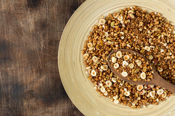 Homemade granola made from buckwheat. Organic buckwheat granola, green buckwheat sprouts, hazelnuts, pumpkin seeds, flax seeds and nutmeg. Granola in a wooden plate on a wooden table. Close-up