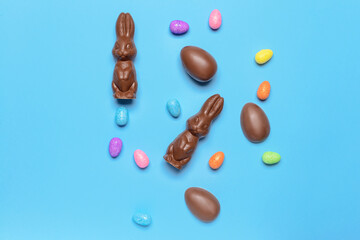 Tasty chocolate Easter bunnies and eggs on color background