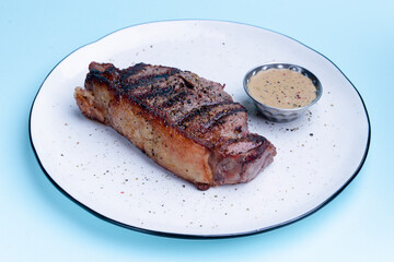 Delicious beef steak with sauce served on a white plate over pastel blue background. BBQ meat, barbecue concept.
