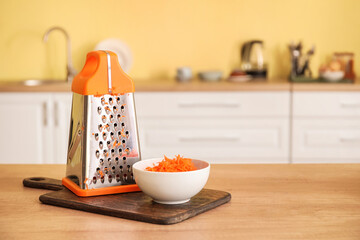 Bowl with grated carrots and grater in kitchen