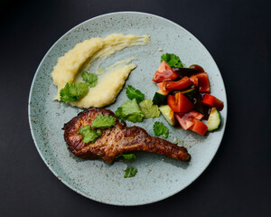 Barbecue Tomahawk Steak with mashed potatoes and vegetables. Served on a blue plate over black background.