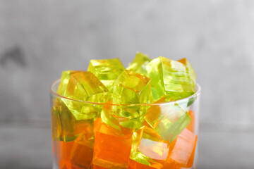 Glass with tasty jelly cubes on grunge background, closeup