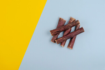 Dried natural healthy treats for dogs. Beef esophagus sticks on a yellow and blue background.