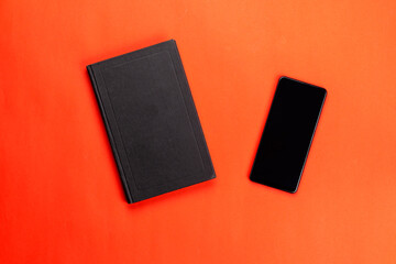 Black smartphone and closed paper book on a red background.