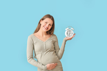 Pregnant young woman with clock on color background