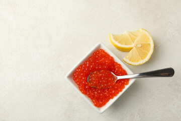 Bowl with caviar and spoon, and lemons on white textured background