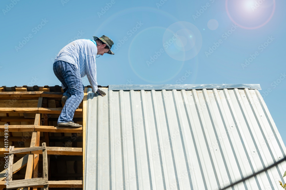 Wall mural carpenter repairs the roof of the house, attaches metal galvanized sheets in hot weather in the brig