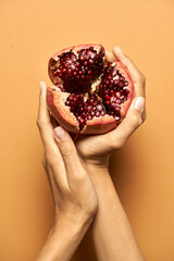 Best taste. Top view of female hands holding opened red fresh juicy pomegranate isolated over orange background. Healthy eating concept